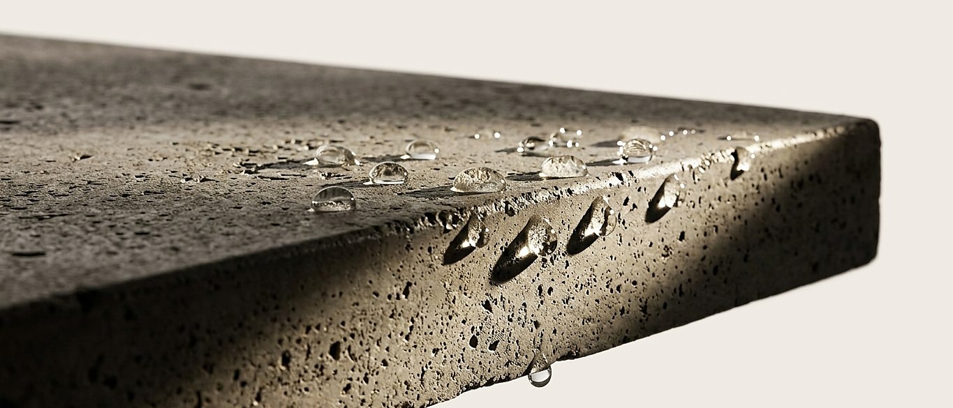 Water beading on the sealed edge of a hand-cast concrete top, raking light picking out the surface texture